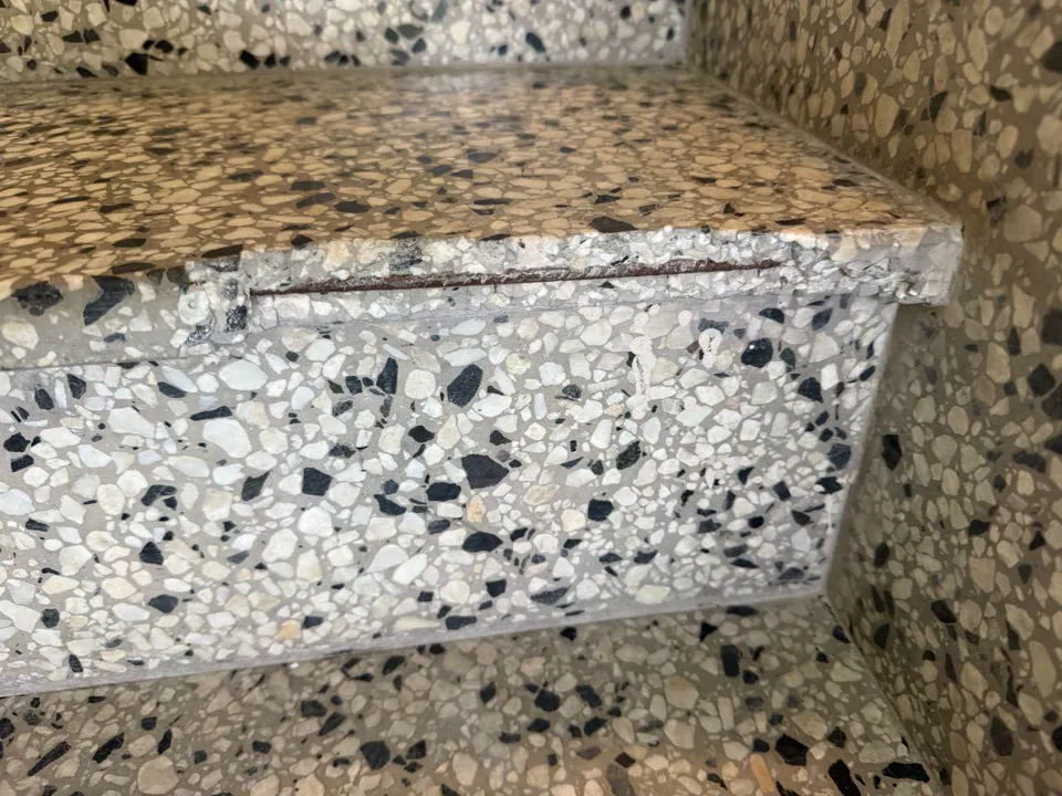 Skadad terrazzotrappa före lagning i Uppsala: sprucken och lös terrazzo i trappsteget